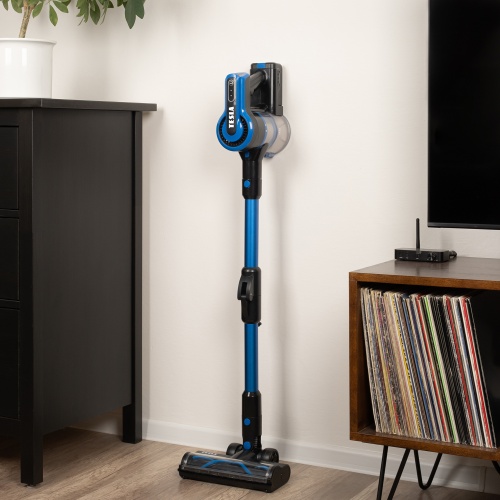 Vysávač TESLA Purestar E70 Aqua Pro parkovaný v stojane vedľa knižnice v minimalistickom interiéri.