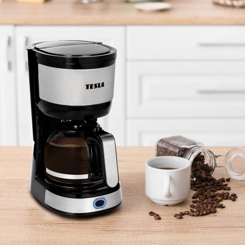 Kávovar TESLA Coffeemaster ES200 v čiernom prevedení na kuchynskej linke s hrnčekom a rozsypanými kávovými zrnami na boku.