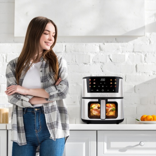 Mladá žena stojaca vedľa multifunkčného teplovzdušného fritovacieho hrnca TESLA AirCook Q60 XXL Pro v modernej kuchyni. Pripravené jedlá vnútri hrnca podčiarkujú jeho univerzálnosť a eleganciu.